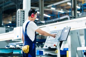 Worker entering data in CNC machine at factory floor to get the production going